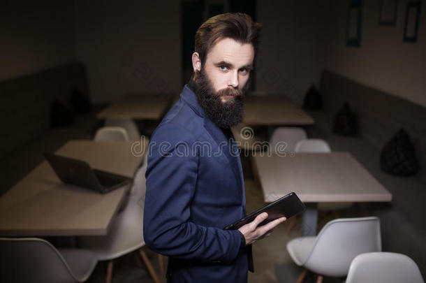 一个留着胡子的男人，穿着西装，在咖啡馆里拿着写字板；