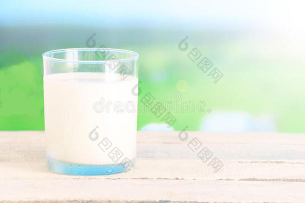 草地上一张白色木桌上的一杯新鲜牛奶。