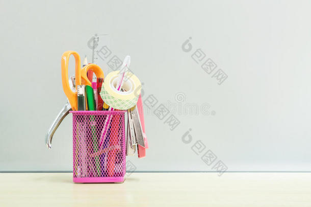 特写办公设备与粉红色钢盒笔在模糊的木桌和磨砂玻璃墙纹理背景在工作中