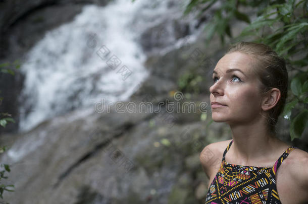 美丽的金发女人的脸特写，仰望着模糊的瀑布