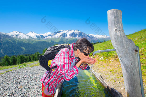 女孩徒步旅行者在爬山时在喷泉处<strong>解渴</strong>