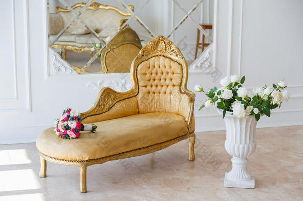 优雅的老式扶手椅在一个宽敞的房间里，墙上装饰着装饰品和镜子。 五颜六色的花插在花瓶上