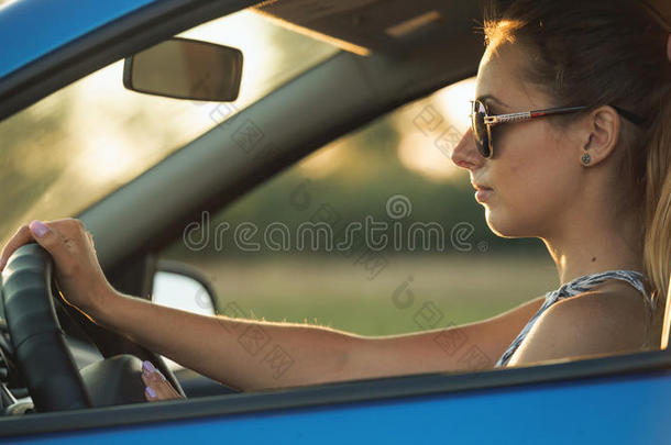 美丽的年轻女人坐在车里，驶进夕阳
