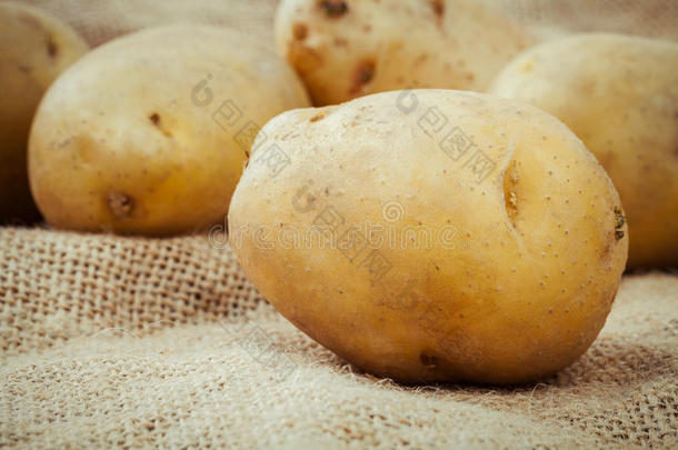 在麻袋背景上特写新鲜有机土豆。 在旧的木制背景上划有机土豆。
