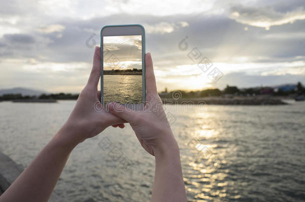 紧紧握住女人的手，拿着智能手机，手机，智能手机在模糊的美丽的大海上，用夕阳的瞬间拍了一张照片
