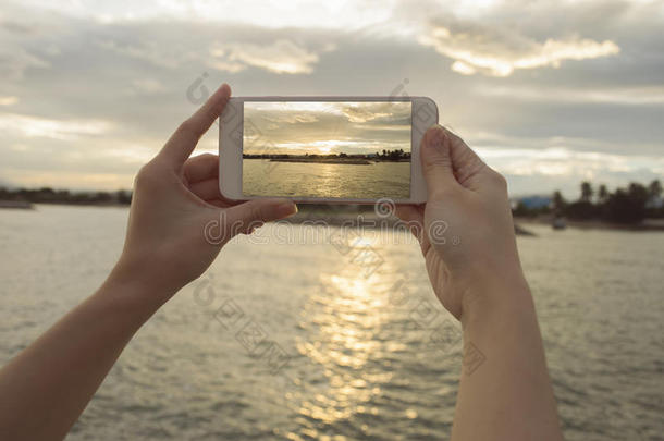 紧紧握住女人的手，拿着智能手机，手机，智能手机在模糊的美丽大海上与夕阳合影