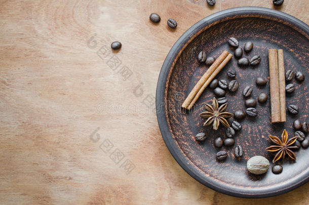咖啡豆，肉桂棒，八角在木制背景上的陶瓷盘子里。