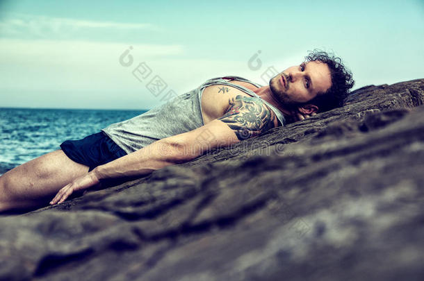 英俊的<strong>肌肉男</strong>在海滩上坐在岩石上