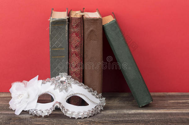 艺术概念。 白色古典狂欢节面具的特写与<strong>复古</strong>书籍和红色背景