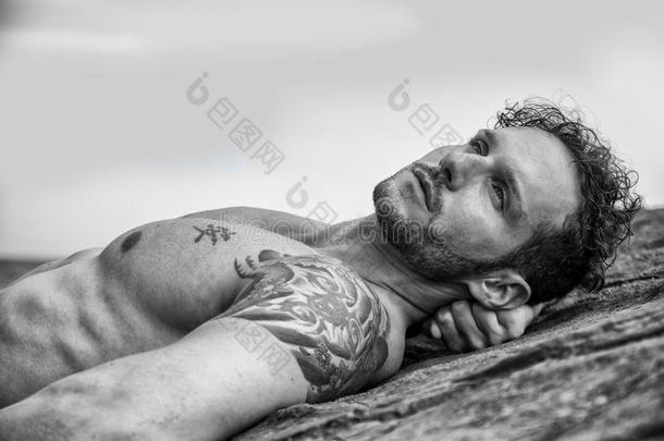 英俊的肌肉男在海滩上躺在岩石上