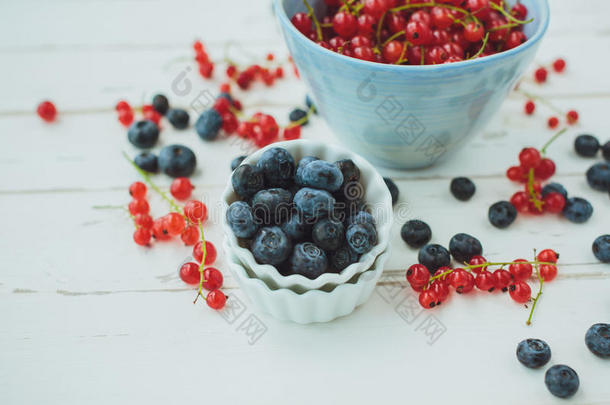 蓝莓和红醋栗放在一个蓝色的桶里，放在一个白色的木头上
