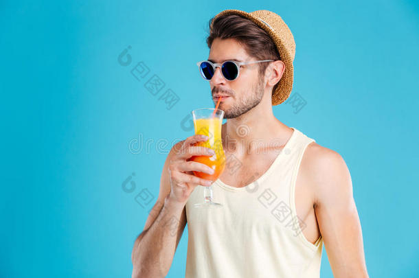 戴着帽子和太阳镜的英俊男人喝着新鲜的橙汁