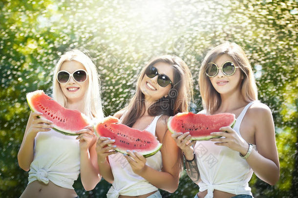 戴着太阳镜的漂亮女孩吃着新鲜的西瓜笑。 快乐的年轻女人在户外拿着西瓜片