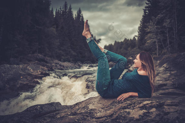 美丽的女人在瀑布附近摆姿势，背景是山林。