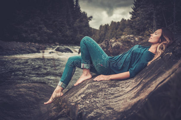 美丽的女人在瀑布附近摆姿势，背景是山林。