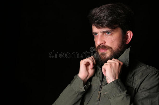 一个留着胡子的男人，穿着卡其色夹克，拿着衣领。特写. 黑色