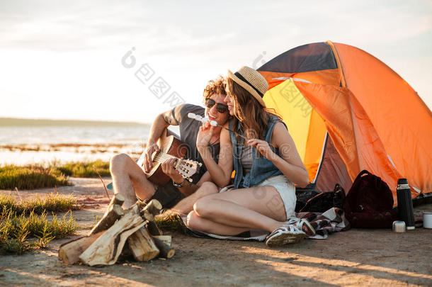 一对夫妇在旅游帐篷附近弹吉他和吃油炸棉花糖