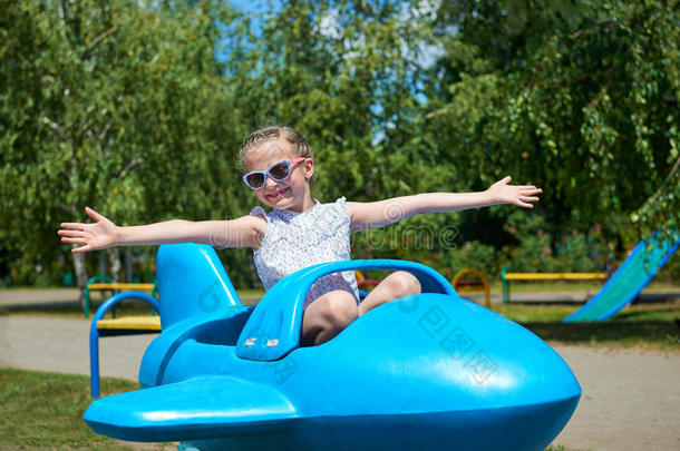 女孩在城市公园的蓝色飞机上飞翔，快乐的童年，暑假的概念