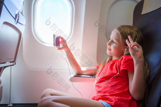 可爱的小女孩乘飞机旅行。 孩子们坐在飞机窗口附近听音乐