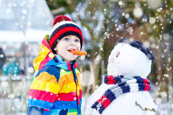 有趣的男孩穿着五颜六色的衣服在户外堆雪人