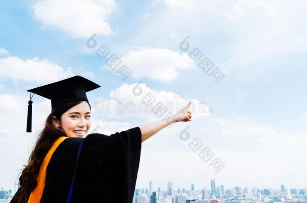 美丽的亚洲大学或大学研究生妇女穿着毕业的学术礼服或长袍，微笑着指着拷贝sp
