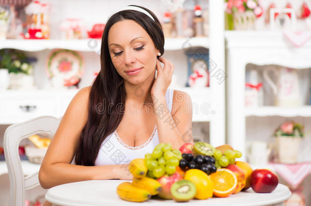 漂亮的黑发女孩坐在厨房的桌子上，拿着<strong>一盘新鲜</strong>的水果。