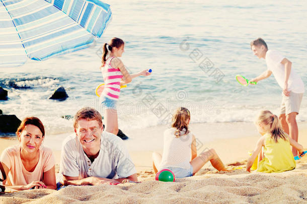 一对夫妇在海滩上放松，而他们的孩子在玩积极的游戏