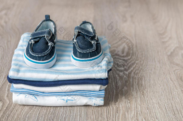 折叠的蓝色和白色紧身衣，上面有灰色的木制背景。 新生儿的尿布。 一叠婴儿衣服。 孩子