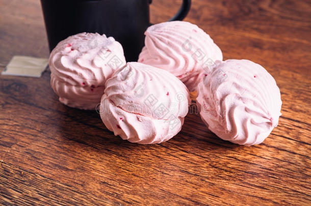几片粉红色的棉花糖和一杯茶在木制的背景上