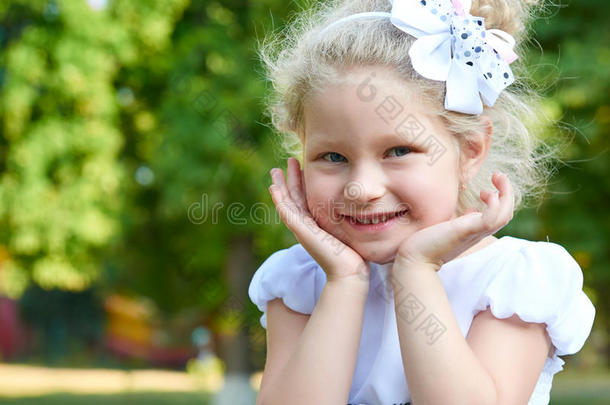 儿童女孩肖像触摸脸特写，摆着白色长袍，快乐的童年概念，夏季在城市公园