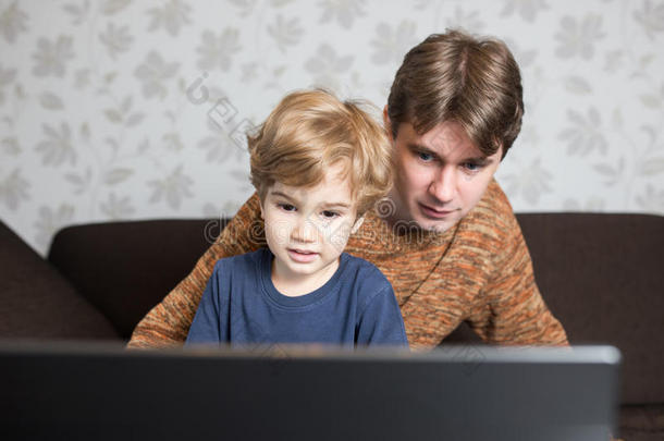 <strong>父亲和儿子在家里</strong>的沙发上一起使用笔记本电脑