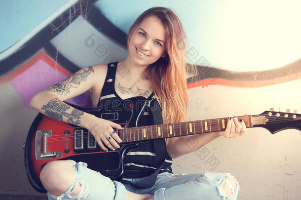 女孩坐在涂鸦墙附近弹电吉他。