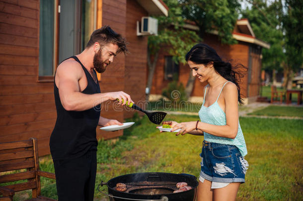 一对夫妇站着做饭，在户外烧烤架上见面