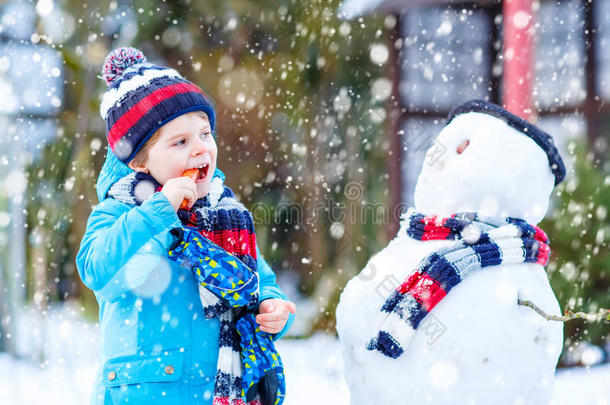 有趣的男孩穿着五颜六色的衣服在户外堆雪人