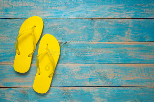 触发器，凉鞋，夏天。 蓝色木头上的黄色拖鞋凉鞋