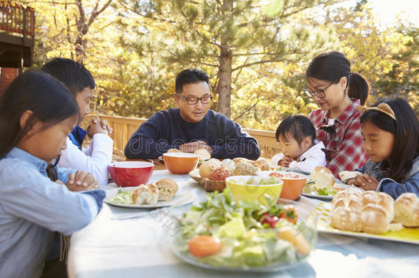 在甲板上的一张桌子上的亚洲家庭在吃饭前祈祷