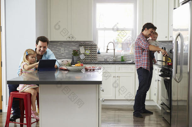 女孩和爸爸一起在厨房用平板电脑，而其他爸爸做饭