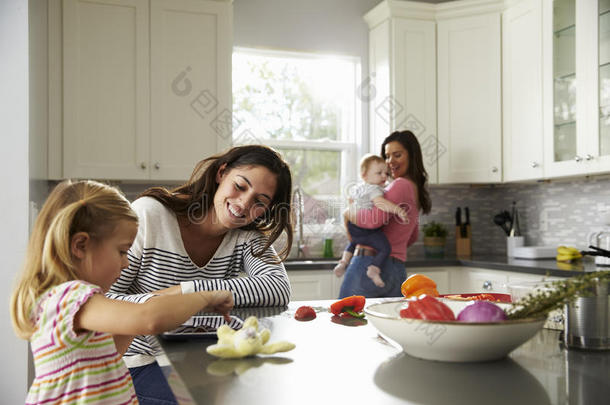 女孩在厨房里和<strong>妈妈</strong>一起用平板电脑，其他<strong>妈妈抱</strong>着孩子