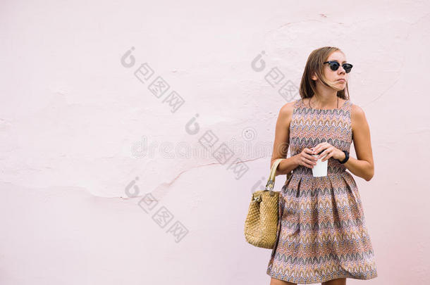 优雅的年轻女人带着咖啡走在淡粉色的墙上