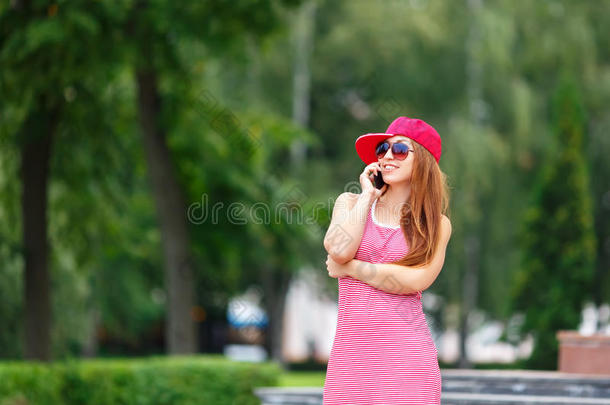 时尚城市肖像时尚时髦的女人说话手机，红色条纹连衣裙，红色帽子和运动鞋，化妆