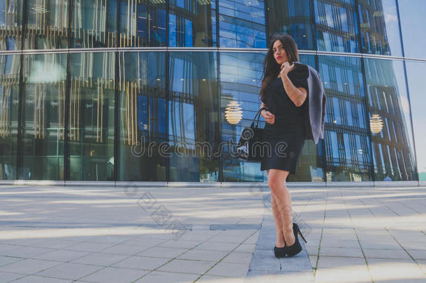 穿着黑色连衣裙的漂亮女孩，手拿钱包和夹克在商务中心的背景上