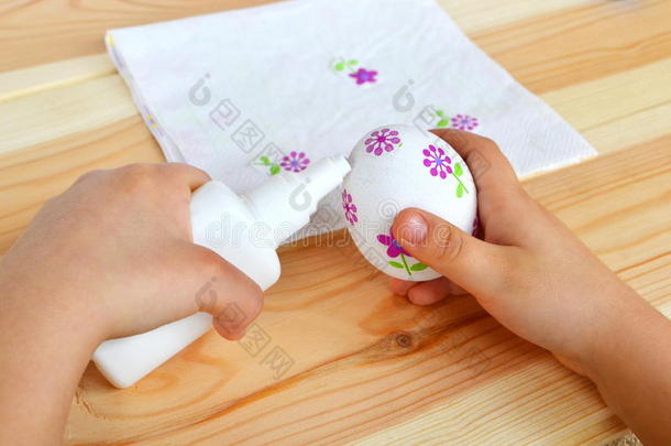 孩子手里拿着一个双层复活节彩蛋和胶水。 孩子把餐巾纸的花片粘在鸡蛋上。 复活节装饰