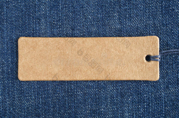 蓝色牛仔布上的空白纸标签。 牛仔裤背景与销售或价格标签。