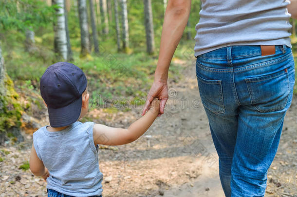 可爱的小男孩牵着父母的手走在公园里。 幸福的家庭和生活方式的概念