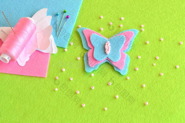 毛毡蝴蝶，纸模板，线，针，别针，珠子，蓝色和粉红色的床单在绿色背景上。 缝纫集，教程