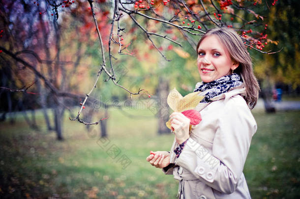 秋天的女人在秋天的公园里快乐地环顾四周，在美丽的五颜六色的森林树叶上微笑