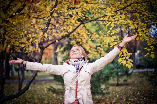 秋天的女人在秋天的公园里快乐地环顾四周，在美丽的五颜六色的森林树叶上微笑