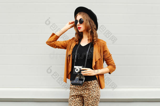 时尚的外观，相当酷的年轻女子模特与<strong>复古胶卷</strong>相机戴着优雅的帽子，棕色夹克在户外的城市背景