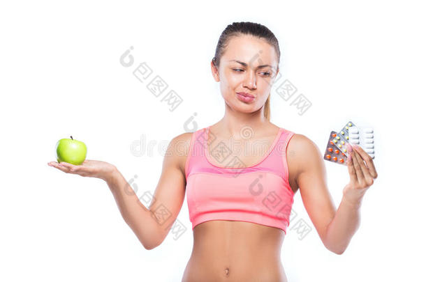 一只手拿着药丸的健身女人，另一只手拿着绿苹果