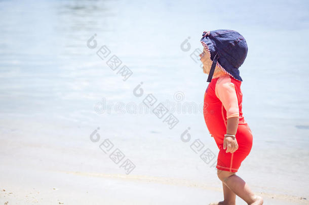 欢快的笑宝宝穿着明亮的太阳防护服，在海滩上奔跑，<strong>背景</strong>是<strong>大海</strong>